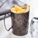 A Libbey hammered antique copper Moscow Mule mug filled with a drink on a table with a cup of french fries.