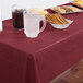 A table with a burgundy Creative Converting plastic tablecloth, food, and drinks including a glass of ice.