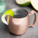 A Libbey copper mini Moscow Mule mug filled with liquid and a lime wedge.