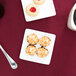 A Libbey Ultra Bright White coupe square porcelain plate with coconut cookies and a cup of coffee on a table.