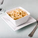 A Libbey square porcelain bowl filled with bouillon soup and noodles with a spoon.