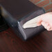 A hand pulling a tissue paper out of a black San Jamar countertop napkin dispenser.