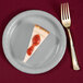 A piece of cheesecake with strawberry jam on a Creative Converting shimmering silver paper plate.