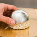 A hand using an Ateco stainless steel hemisphere food mold to shape a rice ball.