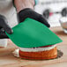 A person wearing black gloves uses Satin Ice Green Vanilla Rolled Fondant to cover a cake.
