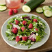 A Carlisle smoke melamine salad plate with a salad of lettuce, raspberries, and cucumbers.
