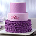 A purple tiered cake with pink ruffles on a plate.