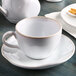 A Tuxton white china saucer with a white cup on a table.