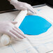 A person wearing a white glove rolling out blue dough on a white surface with a blue circle.