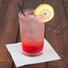 A Spiegelau highball glass with a pink drink, ice, and a lemon slice.