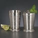 Two World Tableware stainless steel mint julep cups filled with ice and mint leaves next to a lime wedge.