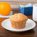 A muffin on an Arcoroc white porcelain plate next to an orange.
