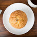 A muffin on a white Arcoroc porcelain plate next to a cup of coffee.