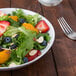 A white deep porcelain plate with a bowl of salad with strawberries, blueberries, oranges, and nuts.