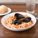 A bowl of spaghetti with mussels and sauce on a white Arcoroc porcelain plate with a glass of water.