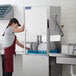 A woman in a red apron using a Jackson TempStar door type dish washer to wash plates in a professional kitchen.