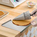 A metal waffle cone forming tool being used to shape a flat waffle into a cone.