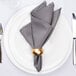 A white cloth napkin on a white plate with a gold napkin ring and silverware.