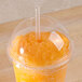 A Fabri-Kal Greenware clear plastic dome lid with a straw in it over an orange drink.