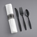 A Visions white pre-rolled napkin with black plastic fork, knife, and spoon on a gray table.