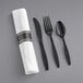 A white pre-rolled napkin with black plastic cutlery on a gray table.