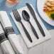 A Visions white pre-rolled napkin with black heavy weight plastic cutlery including a fork, knife, and spoon.