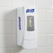A white Purell manual hand sanitizer dispenser on a tile wall.