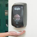 A person holding a GOJO black touchless hand soap dispenser.