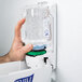 A hand holding a Purell bottle of hand sanitizer in front of a dispenser.