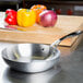 A Vollrath stainless steel saute pan on a counter with red and yellow bell peppers.