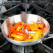A Vollrath Miramar saute pan filled with peppers and onions on a stove.