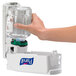 A hand using Purell foaming hand sanitizer to dispense clear liquid into another clear bottle.