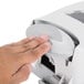 A hand pressing a button on a gray GOJO manual hand soap dispenser.