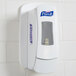 A white GOJO True Fit wall plate for a hand sanitizer dispenser on a white tile wall.