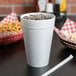 A white Dart foam cup with a lid and a straw filled with ice and soda.