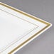 A Fineline Silver Splendor ivory plastic square plate with gold bands on a table.