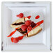 A Fineline white plastic square plate with silver bands holding a piece of cheesecake with raspberries on top.