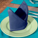 A folded royal blue Intedge cloth napkin on a plate with silverware.