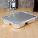 An 8 1/2" x 6 3/8" foil tray with three compartments and a board lid on a table.
