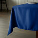 A royal blue Intedge square tablecloth on a table with a white plate on it.