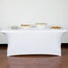 A wood table with white Snap Drape spandex table cover with plates and bowls of food.