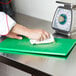 A person using a Carlisle cutting board refinisher to grind food on a green cutting board.