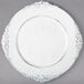 A white Charge It by Jay plastic charger plate with a decorative border.