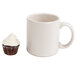 A white cupcake in a Hoffmaster white fluted baking cup next to a white mug with a handle.