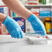 A person in blue Noble Products powder-free disposable gloves cutting pills on a white plate.