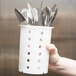 A person holding a white Metro container with holes full of silverware.