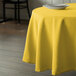A round table with a yellow Intedge tablecloth on it with a white plate.