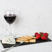 A GET Madison Avenue faux slate melamine display board with cheese, strawberries, and wine.