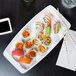 A white Arcoroc china tray holding sushi and chopsticks on a table.