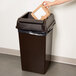 A person putting a piece of paper into a brown Continental Swingline trash can with a lid.